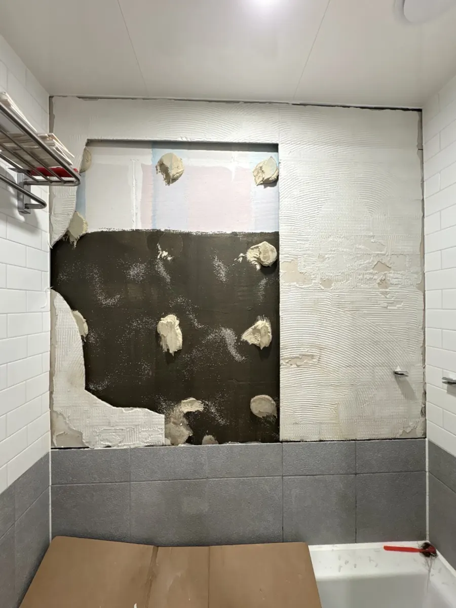 화장실타일깨짐 관련 안내, 욕실 타일 부분 교체 — 욕실 벽 한 구간의 타일을 떼어내 어두운 바탕면이 드러난 모습